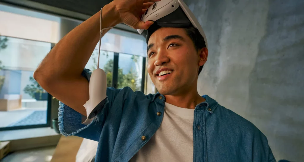 A man lifting up the Meta Quest 3 goggles onto his forehead. A controller is dangling from his wrist. Image source: Meta